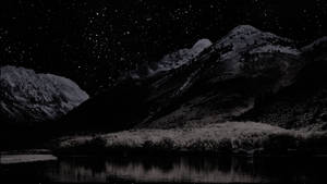 積雪的山脈和結霜的樹木，星空夜空倒映在平靜的湖面上。 — macOS 壁紙