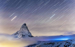 白雪覆蓋的山峰，星軌在夜空雲層上方劃出弧線。 — 瑞士阿爾卑斯山 壁紙