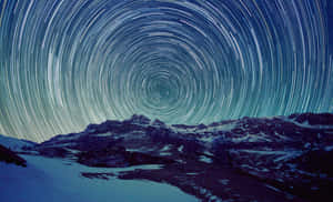 星軌在深藍色夜空下，在積雪的山脈上方旋轉。 — 星星 壁紙