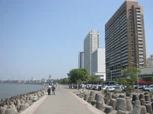 城市海濱步道，旁邊有高樓大廈和水面，還有行人和車輛。 — 孟買 壁紙