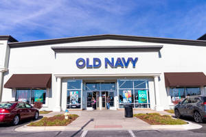 Old Navy 商店入口，陽光普照的日子裡有購物者和停放的汽車。 — 海軍藍 壁紙