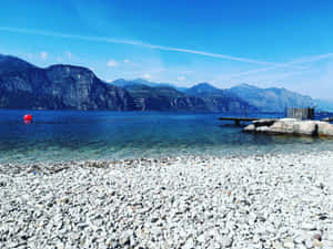 鵝卵石海灘，清澈的藍色海水和山脈在背景中。 — 海灘 壁紙