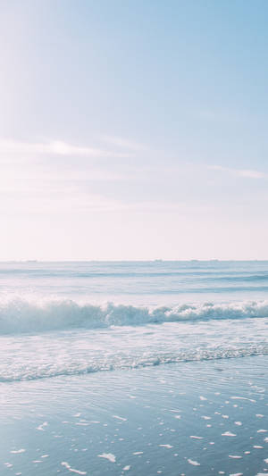 晴朗藍天下，平靜的海浪沖刷著沙灘。 — 美學嬰兒藍 壁紙