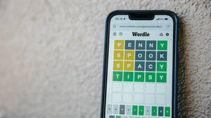 智慧型手機在紋理牆上顯示Wordle遊戲及已解決謎題。 — 8K 手機 壁紙