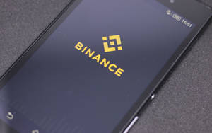 智慧型手機在深色螢幕上顯示 Binance 加密貨幣交易所標誌。 — 簡約手機 壁紙