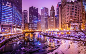 夜晚的城市天際線，燈火通明的建築物倒映在結冰的河流中。 — 城市燈光 壁紙