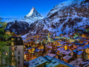 暮色天空下，馬特洪峰與閃爍窗戶的白雪覆蓋阿爾卑斯山村。 — 冬季風景 壁紙