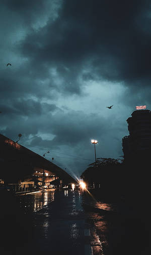 暴風雲下，發光街燈和鳥兒飛翔的黑暗雨夜城市街道。 — 悟空黑 iPhone 壁紙