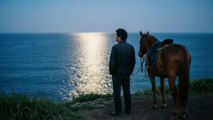 男人和馬站在懸崖上俯瞰月光下的海洋 — 對馬戰鬼 壁紙