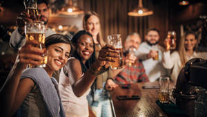一群朋友在酒吧櫃檯前用啤酒乾杯。 — 麥迪遜·比爾 壁紙