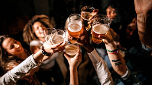 一群朋友在昏暗的派對環境中舉起啤酒杯乾杯。 — 酒吧 壁紙