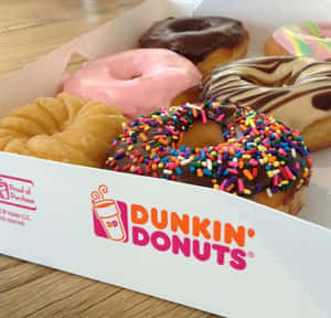 一個裝滿各種彩色灑糖粒和糖霜的Dunkin' Donuts盒子放在木質表面上。 — Dunkin Donuts 壁紙