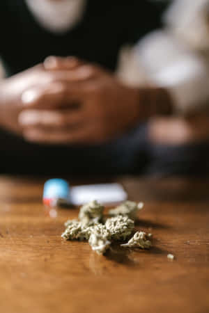 木桌上大麻花蕾和打火機，背景有模糊的手。 — Huawei MatePad 12 X (2025) 壁紙