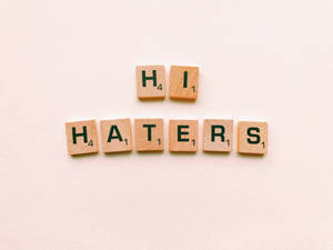 木製 Scrabble 字母牌在米色背景上拼出「Hi Haters」。 — 簡約 壁紙