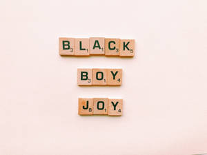 Scrabble 字母磚排列在米色表面上拼出「Black Boy Joy」。