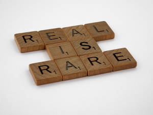 木製 Scrabble 字母磚以填字遊戲佈局拼出 REAL 和 RARE。 — 語錄 壁紙
