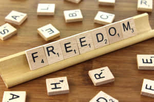 木架上拼出 freedom 的 Scrabble 字母磚，周圍散落著字母磚。 — 自由 壁紙