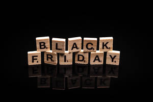 黑色反光表面上用木製Scrabble字母牌拼出的Black Friday。 — 黑色星期五 壁紙