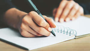 手在螺旋筆記本上書寫於木製書桌。 — 黑白藝術 壁紙