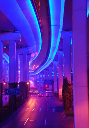 夜晚，藍色和紫色霓虹燈照亮的高速公路，汽車在混凝土高架橋下行駛。 — 霓虹 壁紙