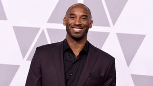柯比·布萊恩身穿黑色西裝在圖案背景上對鏡頭微笑 — 科比· Bryant 壁紙