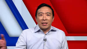 身穿淺藍色襯衫的男子在紅、白、藍色攝影棚背景前發言。