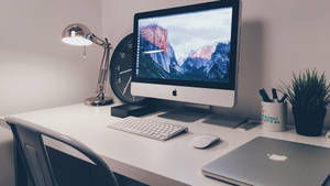極簡居家辦公室桌面，配備 iMac、燈和植物，柔和燈光下。 — 桌面 壁紙