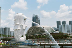 魚尾獅雕像在新加坡城市景觀中噴水，有人和圓頂建築。 — 香港 壁紙