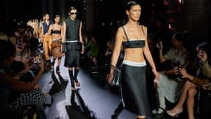 模特兒身穿黑色服裝走在時裝伸展台上，觀眾在拍照。 — 伸展台 壁紙