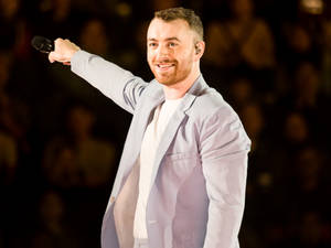 Sam Smith 在舞台上手持麥克風表演，並向觀眾微笑。 — 山姆·史密斯 壁紙