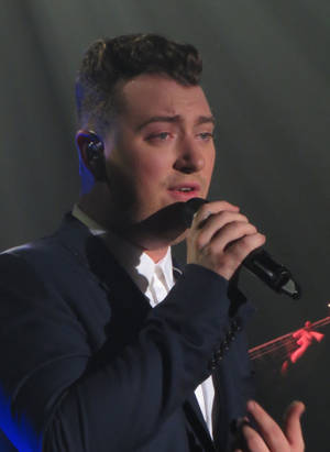 Sam Smith 在燈光璀璨的舞台上對著麥克風唱歌。 — 山姆·史密斯 壁紙
