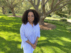 歐普拉·溫芙蕾（Oprah Winfrey）身穿條紋襯衫，在陽光明媚的草坪樹下微笑。 — 歐普拉·溫芙蕾 壁紙