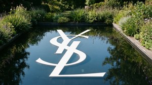 YSL標誌倒映在水中，背景為花園景色。