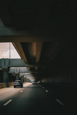 汽車穿過陰暗的混凝土高速公路隧道，駛向明亮的出口。 — 汽車 iPhone 壁紙