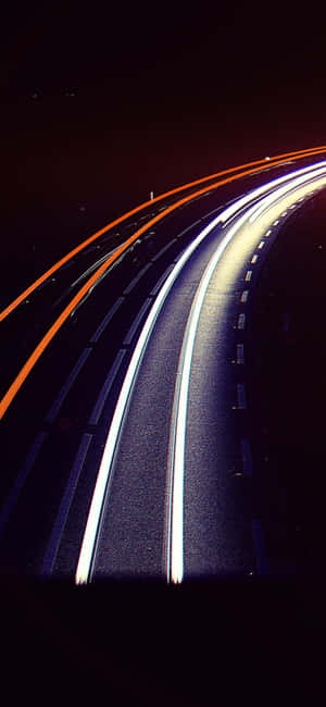 夜間黑暗蜿蜒道路上移動汽車產生的白色和橙色光條。 — iPhone Air 壁紙