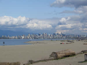 沙灘上有木頭和遠處城市天際線，多雲天空 — 海灘日落 壁紙