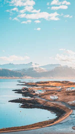 沿海村莊，房屋沿著平靜的海灣，遠處有積雪的山峰。 — 冰島 壁紙