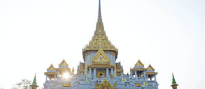 金色泰國寺廟尖塔，中央塔樓後方有陽光四射，映襯著明亮的天空。 — 會長是女僕大人 壁紙