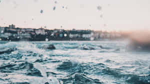 日落時分，海浪拍打著水花，沖向模糊的沿海小鎮。 — 海灘桌面 壁紙