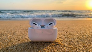 夕陽下沙灘上充電盒中的白色耳機與海浪。 — AirPods 壁紙