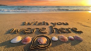 日落時沙上寫著「Wish you were here」，伴有貝殼和對話框。 — WhatsApp 壁紙