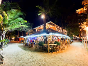 夜晚海灘酒吧，棕櫚樹和客人在燈串下享用飲品。 — 海灘 壁紙