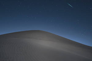 繁星點點的夜空下，沙漠沙丘上流星劃過天際。 — 攝影 壁紙