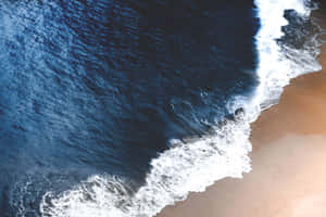 海浪與沙灘相遇並帶有白色泡沫的航拍照片。 — 沙漠 壁紙