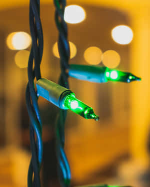 溫暖室內環境中發光綠色串燈，帶有扭曲的黑色電線。 — 4:5 壁紙