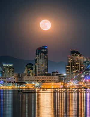 夜晚城市上空的滿月，燈光在水面上反射。 — 城市燈光 壁紙