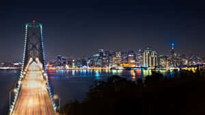 夜間城市景觀，包括燈火通明的灣區大橋和舊金山天際線，水面上的光跡。 — 舊金山 壁紙