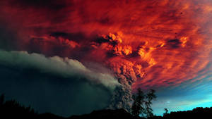 火山爆發，熾熱的紅色火山灰映襯著暮色天空和樹木剪影。 — 煙動圖 壁紙