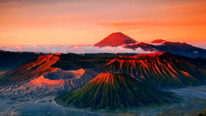 火山沐浴在橙色日出光中，下方有雲。 — 印尼 壁紙