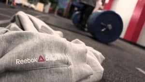 灰色 Reebok CrossFit 運動衫放在健身房地板上，靠近槓鈴。 — 低調 壁紙